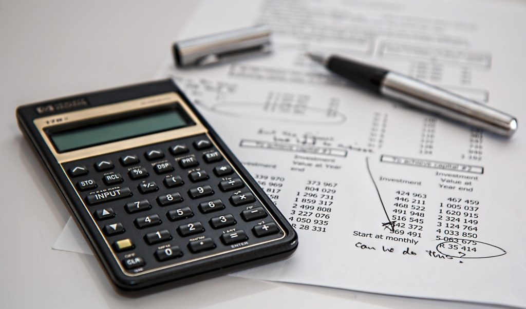 A black calculator and an open pen on top of a financial sheet